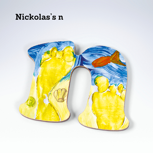 The letter N with a hand painted beach appterns showing footprints in the sand, shells and a fish in blue sea.