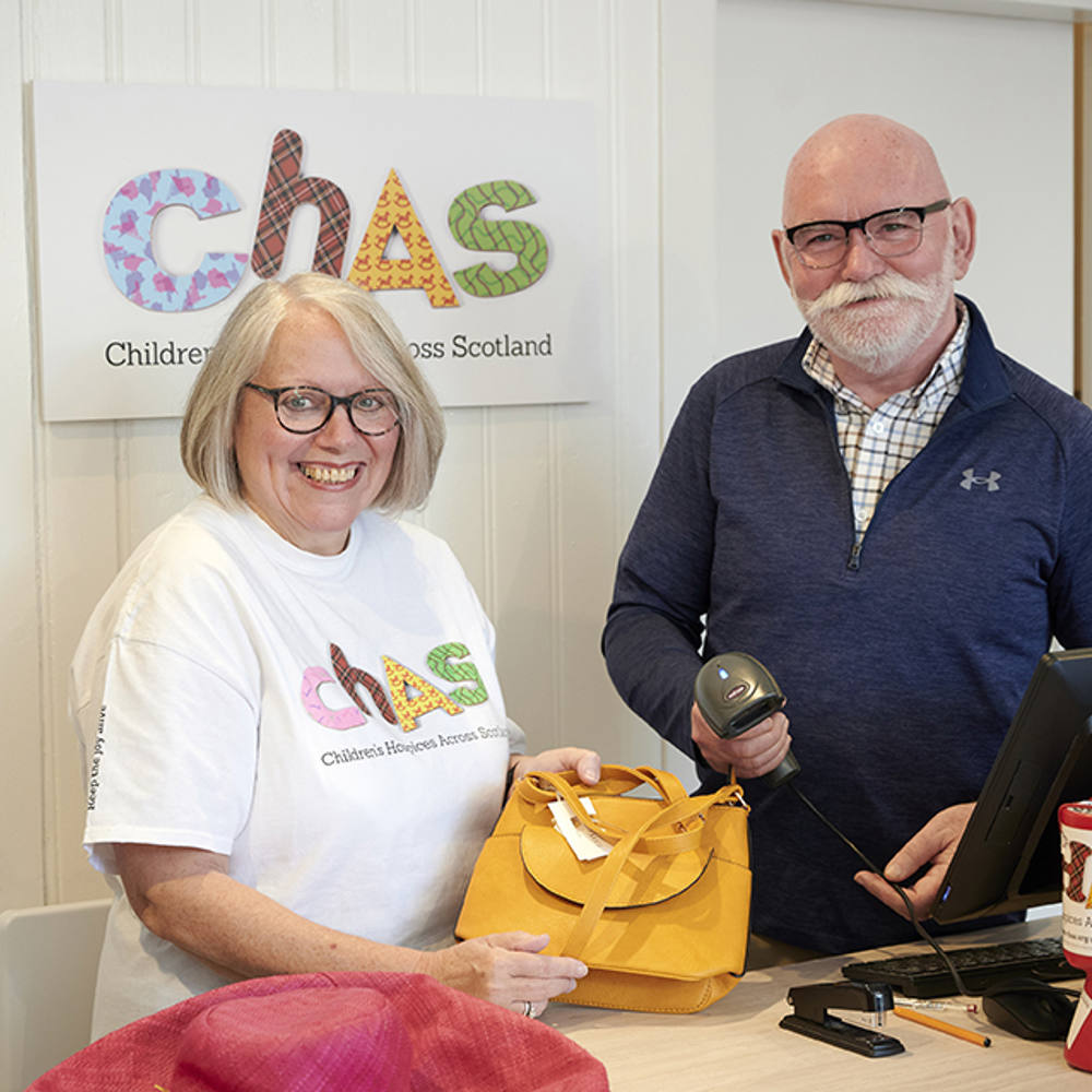 A woman shop volunteer holds a bag as a male volunteer scans the price tag.